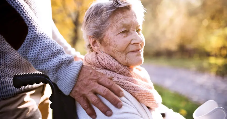 Seniorin im Rollstuhl mit Betreuungskraft im Herbstpark