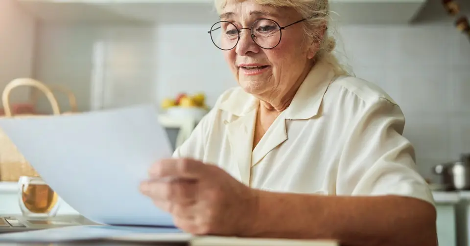 Seniorin liest Unterlagen am Küchentisch