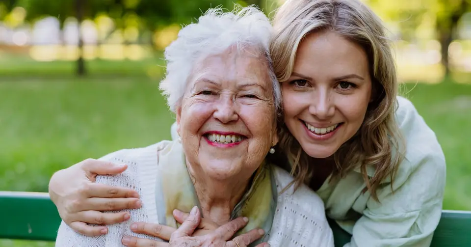 Seniorin und Betreuungskraft lachen zusammen im Garten